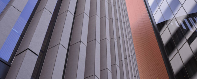 Upward view of a modern building façade with vertical metal fins forming a cassette-style sunshade system.