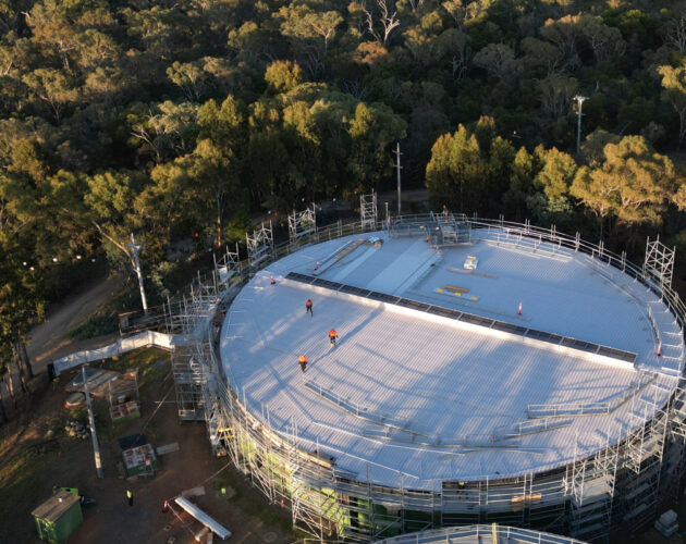 Aerial drone view of the covered Red Hill Reservoir in the ACT, showing two large circular reservoir cells surrounded by dense bushland.