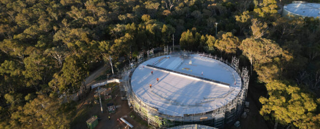 Aerial drone view of the covered Red Hill Reservoir in the ACT, showing two large circular reservoir cells surrounded by dense bushland.
